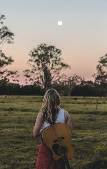 Woman with guitar in field at dusk